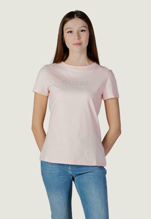 T-shirt in cotone rosa chiaro con maniche corte, scollo rotondo e logo "GUESS" argento sul davanti. Abbinata a jeans blu.