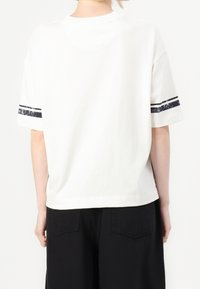 Bílý bavlněný tričko s krátkými rukávy, má modré pruhy podél rukávů. Pohodlný střih, zadní pohled ukazuje jednoduchý design.