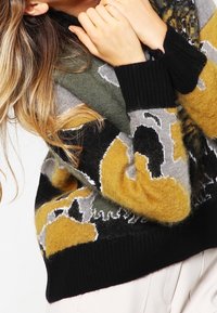 Gestrickter Pullover in Schwarz, Grau und Senfgelb mit geometrischem Muster. Verfügt über einen breiten, gerippten Rundhalsausschnitt und Bündchen und besteht aus einer strukturierten Wollmischung.