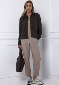 Camicia a quadri marrone con bottoni, top aderente beige, pantaloni beige con bottone, borsa marrone e sneakers argento. Texture lisce e stile casual.