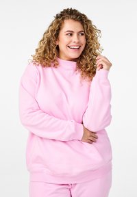 Felpa rosa chiaro con collo alto, maniche lunghe e vestibilità rilassata. Realizzata in morbido tessuto testurizzato, con polsini e orlo a costine.