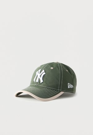 Groene honkbalpet met wit New York Yankees-logo en beige rand, weergegeven op een effen lichtgrijze achtergrond.
