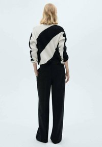 Pull en tricot noir et blanc avec un motif diagonal, associé à un pantalon noir taille haute. Le pull a des manches 3/4.