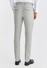 Jasnoszare, dopasowane spodnie z wzorem w kratę, dwiema tylnymi kieszeniami i smukłym krojem. Wykonane z tkaniny o splocie, uzupełnione czarnym obuwiem.