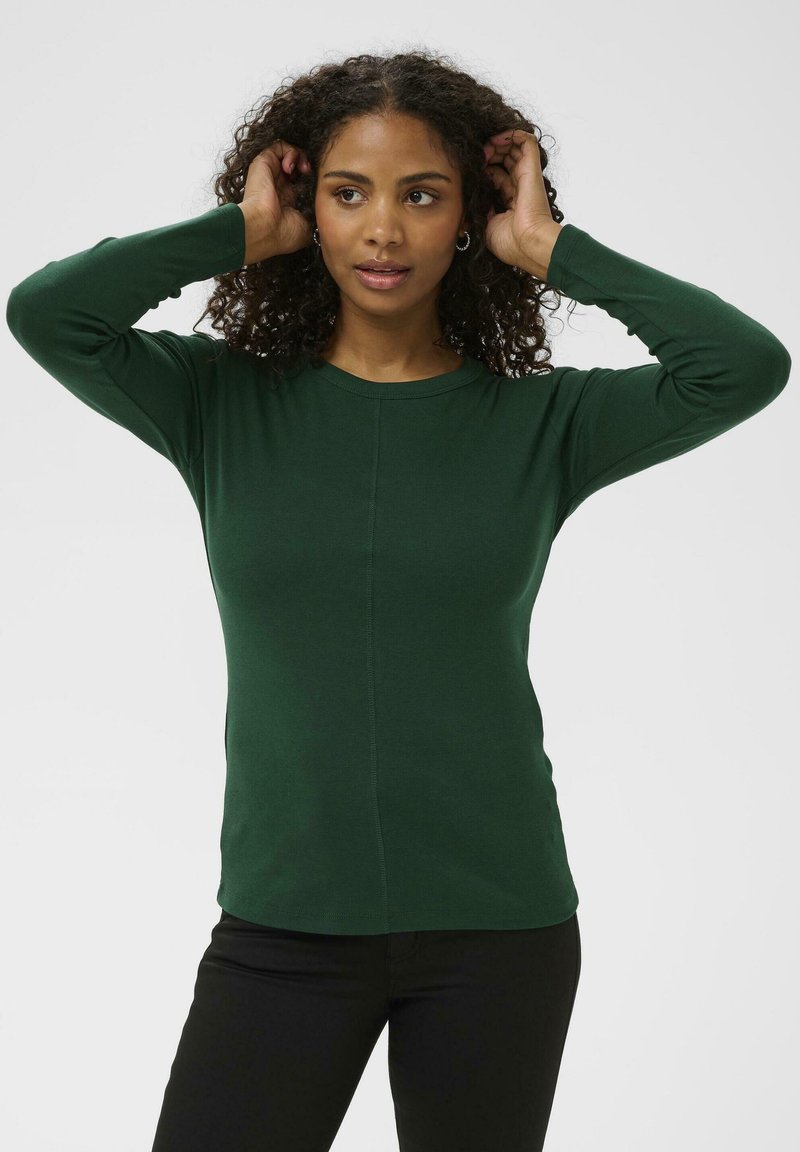 T-shirt vert à manches longues avec un col ras du cou, présentant un design ajusté et une texture subtile, porté avec un pantalon noir.