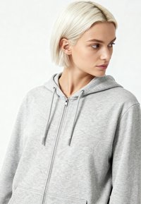 Felpa grigia con zip, tasca anteriore, cappuccio regolabile con coulisse e una sottile texture. Presenta una zip in metallo e accenti argentati.