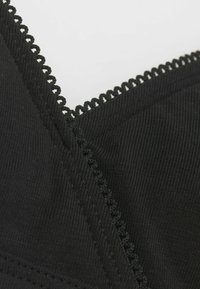 Černá tkaninová podprsenka s texturovaným žebrováním, krajkovým lemem kolem výstřihu a čistým šitím viditelným na švech.