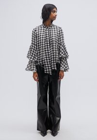 Μπλούζα ασπρόμαυρη με καρό σχέδιο και μανίκια με βολάν, συνδυασμένη με μαύρο βινύλιο παντελόνι ψηλής μέσης και μυτερά τακούνια.