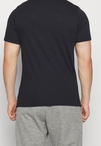 Camiseta de algodón negro de manga corta vista desde la parte de atrás, combinada con pantalones deportivos grises. Presenta un color sólido y un ajuste estándar.