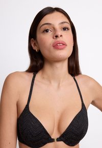 Reggiseno nero con motivo a zigzag e finitura testurizzata. Presenta spalline sottili e una chiusura in metallo dorato sul davanti.