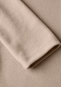 Ribbade beige tyget med en mjuk textur; har en vikt ärm och släta sömmar. Ytan visar fina, parallella linjer.