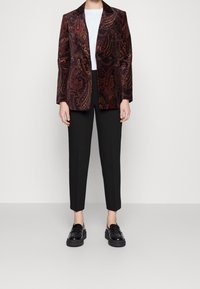 Blazer de terciopelo en burdeos con estampado de cachemira, combinado con pantalones ajustados negros y mocasines negros brillantes. Camiseta blanca debajo.
