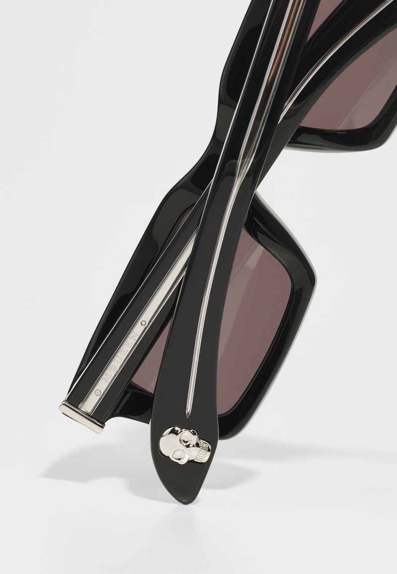 Lunettes de soleil noires avec des montures surdimensionnées, des verres sombres, des accents argentés et un motif de crâne sur la branche. Design élégant avec une finition brillante.