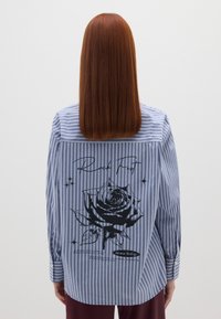 Camicia a righe blu e bianca con una grafica di una rosa nera e testo sul retro, con maniche lunghe e orlo arrotondato.