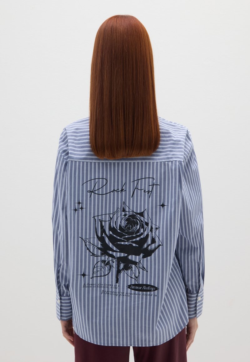 Camicia a righe blu e bianca con una grafica di una rosa nera e testo sul retro, con maniche lunghe e orlo arrotondato.