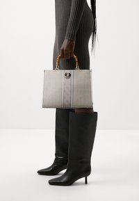 Gray patterned handbag with a structured design, bamboo handles, and a metal accent; paired with tall black leather boots.