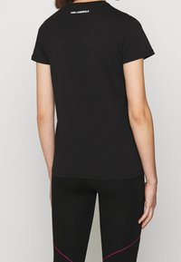 Camiseta negra de manga corta hecha de algodón, con un escote redondeado. Logo "KARL LAGERFELD" en blanco en la parte posterior. Combinada con leggings negros.