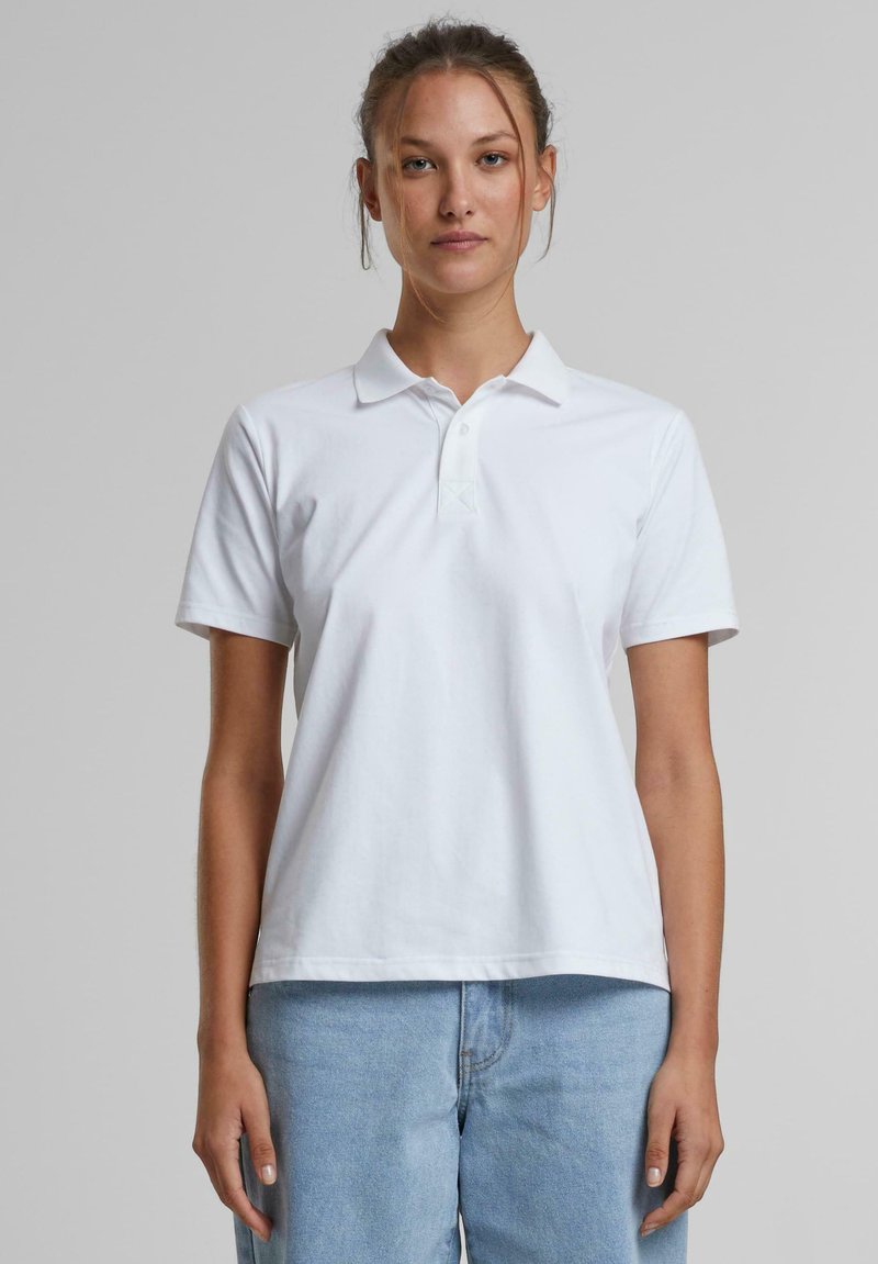 Hvit kortermet polo med krage, laget av bomull. Den har en knapplist og en avslappet passform, kombinert med lyseblå denimbukser.