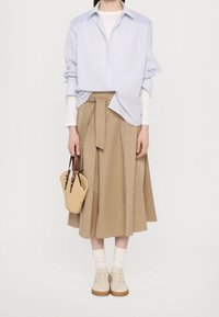 Henkilö, jolla on päällään vaaleansininen raidallinen paita valkoisen pitkähihasen päällä, beige midi-hame, jossa on solmittava vyötärö, valkoiset sukat, beige lenkkarit ja olkahihnalla varustettu olkalaukku.