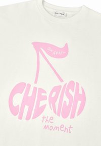 Sweatshirt blanc avec un grand texte graphique rose : "CHERISH" et "le moment", accompagné d'une paire de cerises stylisée et d'une bannière "OH APRIL".