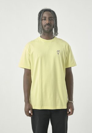 Yellow cotton t-shirt with a round neckline, short sleeves, and a small purple graphic accent on the left chest area.
