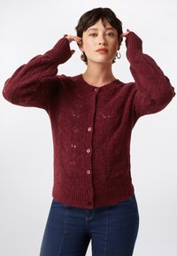 Cardigan en maille bourgogne avec un motif de diamants texturé, des poignets côtelés et cinq boutons avec des accents roses. Manches longues et encolure arrondie.