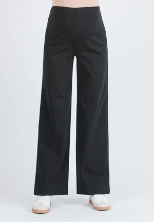 Zwarte wijde broek van zachte stof, met een hoge taille en een gladde afwerking. Gecombineerd met witte sneakers voor contrast.