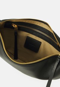 Black leather bag with gold zipper, cream-colored interior, featuring a zipper pocket and a small black leather label inside.