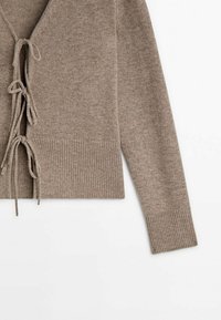 Ruskea neulottu neuletakki v-aukkolla, etusolmituksella ja resorisilla hihansuuilla. Pehmeä pinta ja lyhyt malli.