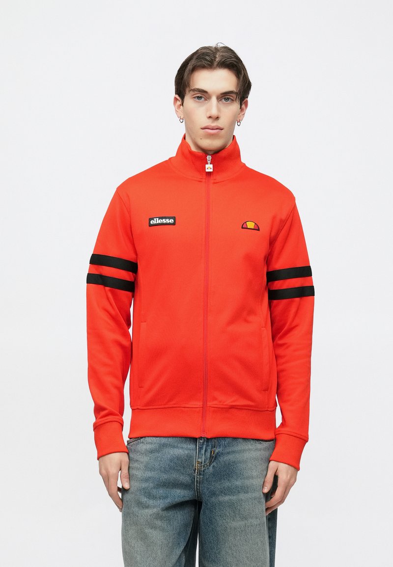 Punane tõmblukuga dressipluus kõrge kraega, mustade triipudega varrukatel, rinnal logomärk, sile tekstuur ja küljetaskud.