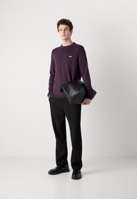 Violeta garā piedurkne krekli ar baltu logotipu, melnas drapētas bikses un melna ādas clutch soma. Gluda auduma un piegriezuma fit.
