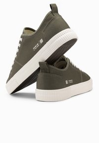 Olivgrüne Leinensneaker mit weißer Gummisohle, Schnürdesign und Logodetail. Verfügt über eine Zuglasche an der Ferse und eine strukturierte Sohle.