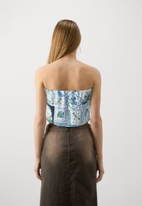 Top senza spalline in motivo floreale blu e bianco, con un corpino aderente. Abbinato a una gonna di jeans marrone con chiusura a zip sul retro.