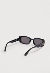 Μαύρα γυαλιά ηλίου με ορθογώνια σκελετά, σκούρους φακούς και ανάγλυφο μοτίβο στα πλαϊνά. Διαθέτουν χρυσή λεπτομέρεια στη μία πλευρά.