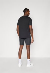 Zwarte T-shirt met korte mouwen en een ronde halslijn, gecombineerd met strakke grijze shorts. Witte sokken en sneakers maken de outfit compleet.