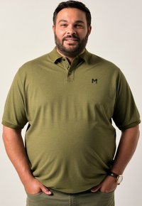 Olivgrön polo skjorta med texturerad tyg, treknappars placket och en liten svart logotyp på vänster bröst. Korta ärmar och avslappnad passform.