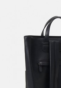 Black leather tote bag with smooth texture, tall rectangular shape, two sturdy handles, and a front pocket with a zipper detail.
