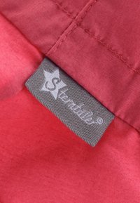 Roter Stoff mit glatter Textur, der ein graues Etikett enthält, das in die Naht genäht ist, mit weißer Markenbeschriftung und Logo.