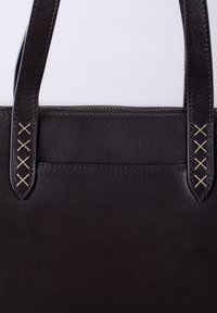 Black leather tote bag with textured surface, featuring two sturdy handles and decorative cross-stitch accents near the handles.
