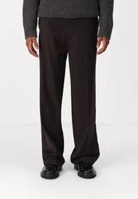 Donkerbruine wijde broek met een gladde textuur, voorzien van een platte voorkant en zijzakken, gecombineerd met zwarte schoenen.