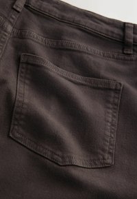 Schwarzer Baumwolldenimstoff, der eine hintere Tasche mit rechteckiger Form, verstärkten Nähten und glatter Textur zeigt.
