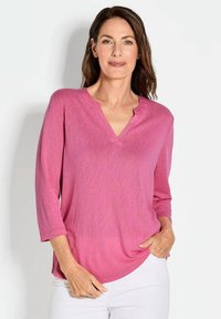 Rosa V-Ausschnitt-Oberteil mit Dreiviertelärmeln, aus einem weichen, strukturierten Stoff gefertigt. Das Design weist einen lässigen Schnitt und einen abgerundeten Saum auf.