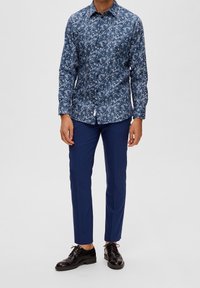 Blå mönstrad skjorta med lång ärm och krage med knappar, i kombination med marinblå tajta byxor och svarta skor. Väl avvägda proportioner och design.