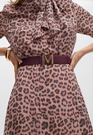 Bluse mit Leopardenmuster und Schleifen-Ausschnitt, getragen mit einem breiten burgunderfarbenen Ledergürtel mit einer goldenen 'M' Schnalle. Strukturierter und gemusterter Stoff.