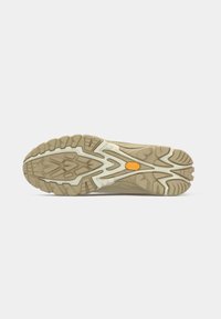 Suola di scarpe da trekking beige con profonde scanalature e accenti bianchi, con un logo Vibram arancione al centro.