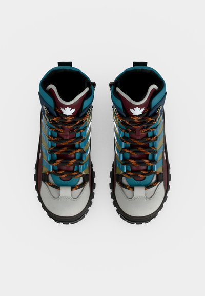 Paire de chaussures de randonnée montantes avec des panneaux turquoise, bordeaux, gris, des lacets noirs et orange, et un emblème feuille d'érable blanche sur la languette.