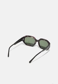Ochelari de soare hexagonali cu o ramă din plastic tortoise închis, lentile verzi și brațe negre. "Vogue" este imprimat pe braț.
