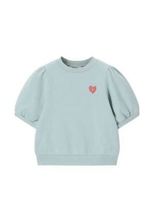 Chemise courte bleu clair à manches bouffantes, avec un col rond et un petit écusson en forme de cœur rouge sur la poitrine gauche.