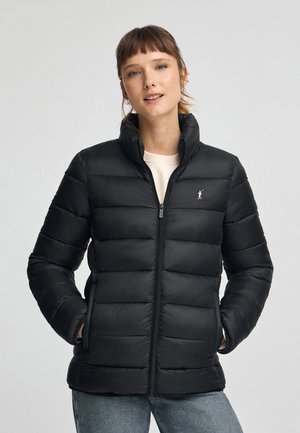 Czarna kurtka puchowa z pionowym pikowaniem, z pełnym zamkiem błyskawicznym i wysokim kołnierzem. Posiada małe logo na lewej piersi.