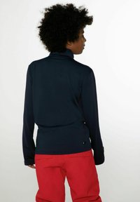 Pullover blu navy a maniche lunghe con colletto alto e fori per i pollici, realizzato in tessuto morbido. Pantaloni rossi in vista, dotati di tasche e dalla vestibilità rilassata.